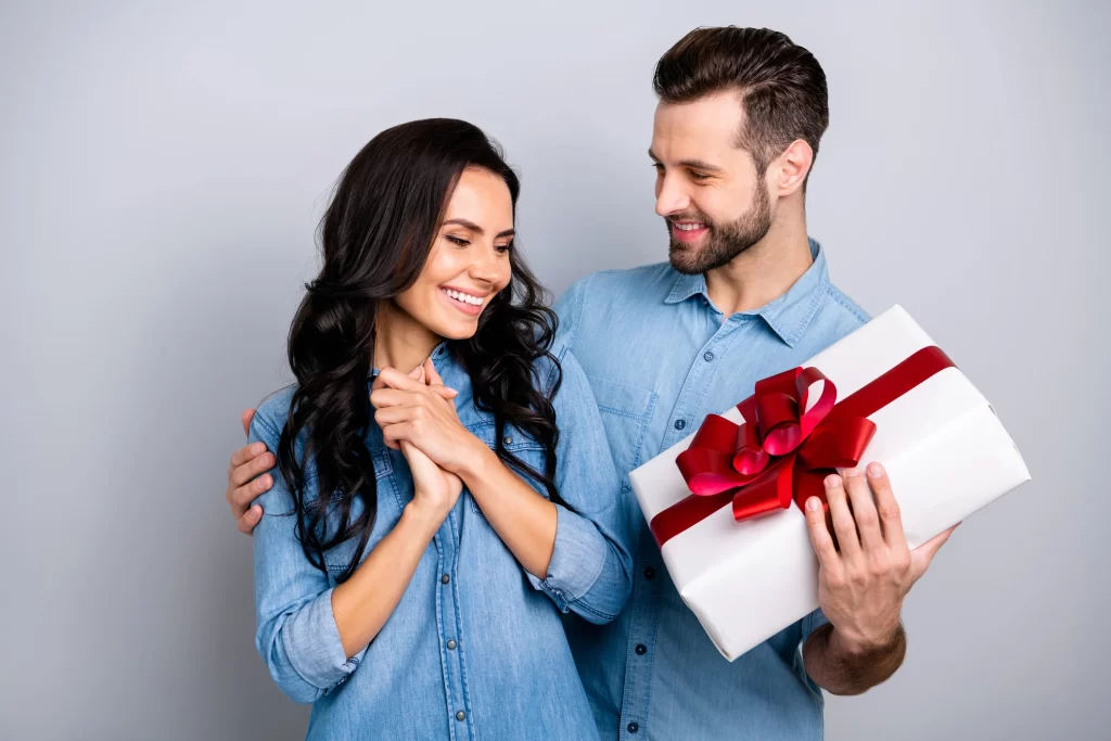 Man surprising partner with thoughtful Valentine’s Day gift wrapped with red ribbon