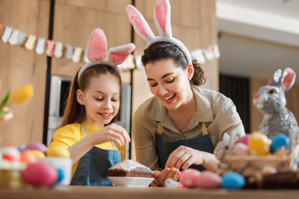 Mother and daughter baking Easter treats with healthy cookware and decorated eggs